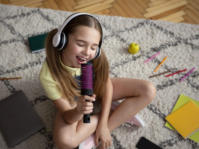 High angle view of charming teenage girl singing using brush as a microphone, wearing headphones, sitting on the floor  Būreliai girl listening to music and singing in brush HYEMQ9C scaled 800x600